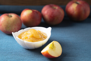 Applesauce, made at home from garden fruits, lies in a white saucepan, next to juicy apples on a blue napkin. Home cooking, copy space..