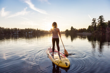Adventurous Caucasian Adult Woman Paddling on a Stand up Paddle Board in water at a city park....