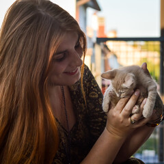 Portrait of a young woman with long red hair playing with a two month old cream colored kitten