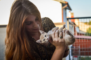 Portrait of a young woman with long red hair playing with a two month old cream colored kitten