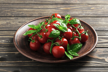 Plate with fresh branches of cherry tomatoes and basil on wooden background