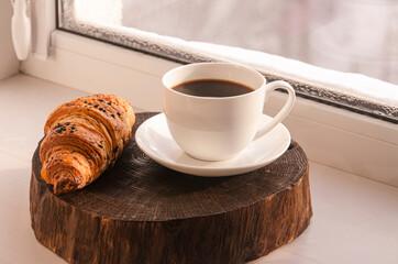 A cozy concept. Classic winter breakfast. A cup of coffee and a croissant stand on the windowsill.