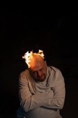 Bald man in a straitjacket with a burning head on a dark background.