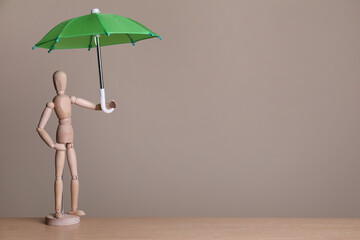 Mannequin holding small umbrella on wooden table. Space for text