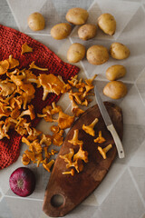 fresh chanterelle mushrooms, potatoes and onion on a wooden cut board with a knife top view