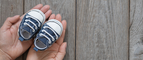 female hands holding little baby shoes banner, tiny sneakers in mom's palms, happy mom's day...