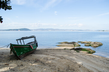 Fototapeta na wymiar Pequeno barco na cor verde em frente a praia. Praia em Paquetá, rio de janeiro.
