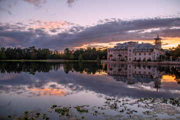 Fototapeta na wymiar A hotel in Celebration (Orlando, Kissimmee), Florida reflects at the edge of a small lake during sunset with interesting cloud formations above.
