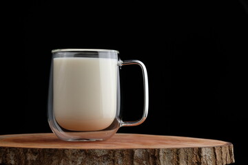 a glass of milk on a wooden coaster on a black background
