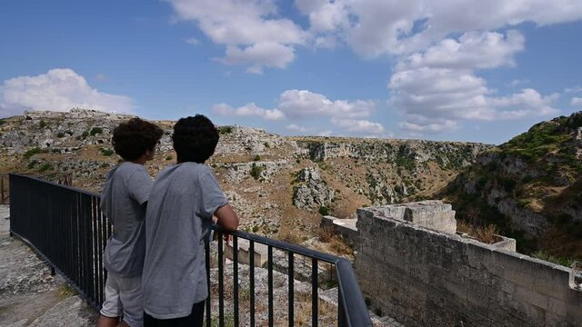 Matera, Basilicata, Italy.August 2021. Footage of two boys admiring the landscape of the cave of Matera and commenting on it pointing to it. Pan movement from boys to landscape,
