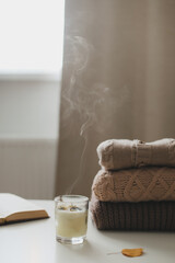 cozy comfortable home autumn still life with a candle, book, knitted sweaters and plaid