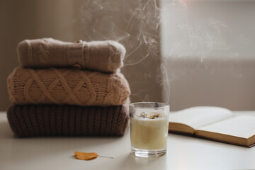 cozy comfortable home autumn still life with a candle, book, knitted sweaters and plaid