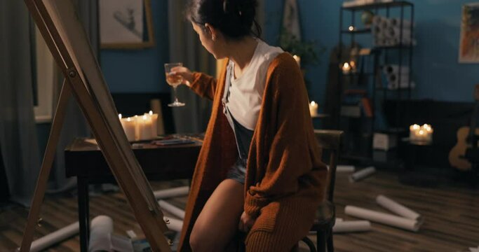 Atmospheric, candles lit in the middle of an easel to which a talented girl approaches, puts down a glass with a drink and begins to sketch with a pencil pulled out of hairstyle