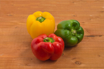 three red, green and yellow peppers isolated on wooden background
