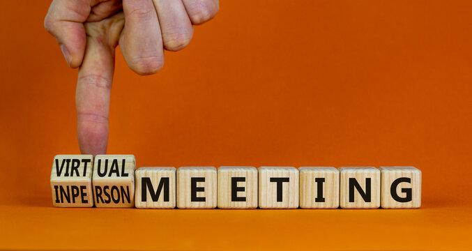 Virtual or inperson meeting symbol. Businessman turns cubes, changes words inperson meeting to virtual meeting. Beautiful orange background. Business, virtual or inperson meeting concept, copy space.