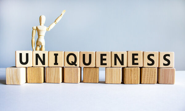 Uniqueness symbol. The word Uniqueness on wooden cubes. Wooden model of human. Businessman icon. Beautiful white background. Business and uniqueness concept. Copy space.