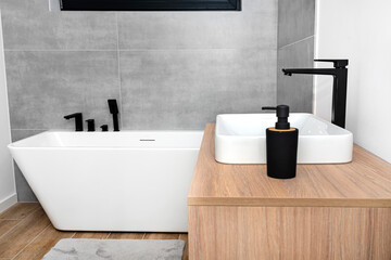 A modern washbasin in the bathroom in a wall mounted cupboard with a matte black faucet, a wall lined with gray ceramic tiles.