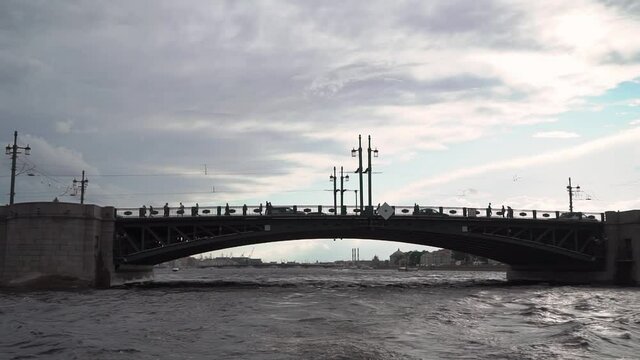 Silhouette of the bridge in the city across the river. Sailing on a ship or yacht on the water under the bridge. People and cars. Drawbridge Palace Bridge in St. Petersburg, Russia.
