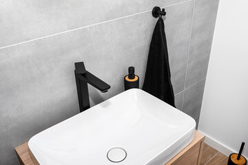 A modern washbasin in the toilet in a wall mounted cupboard with a matte black faucet, a wall lined with gray ceramic tiles.