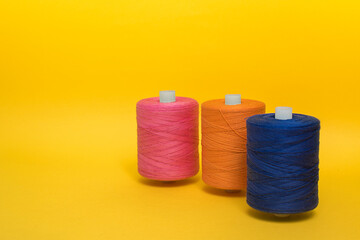 Three multi-colored spools of thread stand one after anothe.