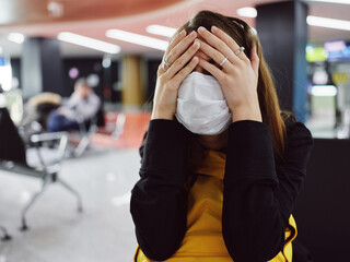 Fototapeta premium woman in medical mask covers her face with her hands fatigue flight delay airport