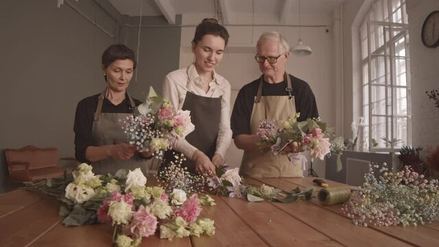 Medium shot of young female florist helping adult man and woman with flower arrangement during floral masterclass in cozy studio