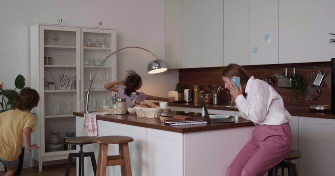 Single mom business woman trying to work talking over phone at home kitchen table while noisy teen children run around.