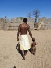Fotobehang Horizontal shot of black-skinned male and child in African clothes, Mafwe stam in Namibia © Leoni Groeneboer/Wirestock