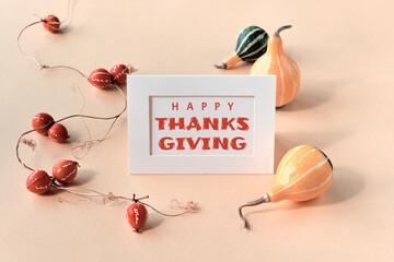 Autumn decorations, text Happy Thanksgiving on craft paper card. Natural decorative Fall pumpkins and red climbing plants. Natural Fall composition in beige, red, orange, cream on paper background.