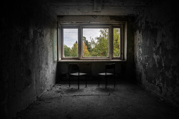 A room with a window and chairs in an old abandoned house. Dirty shabby walls. A tree on the street outside the window. Play of light and shadow. A beautiful abandoned room. Old chairs.