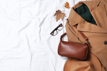 Flat lay composition with stylish hat and autumn clothes on white fabric, space for text
