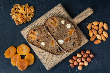 Two slices of bread with nuts and dried fruit on a wooden cutting board, a healthy snack. View from above, dark background.