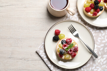 Fototapeta na wymiar Delicious tartlets with berries and tea on light wooden table, flat lay. Space for text