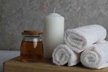 Obraz na płótnie Canvas oil for body massage white candle towels snail on a wooden tray on a gray background side view. Spa relaxation massage. Body care