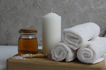 Obraz na płótnie Canvas oil for body massage white candle towels snail on a wooden tray on a gray background side view. Spa relaxation massage. Body care