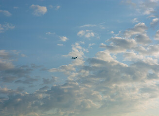 a dark figure of an airplane flying up against a background of blue sky and clouds