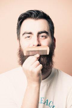 Portrait of bearded barber holding equipments in hand, looking at camera, isolated on pastel background