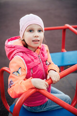 Girl in pink autumn clothes on the playground.