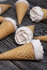 Homemade marshmallows are spread out on the table surface. Zephyr in a waffle cone. Made in the shape of a rose. Close-up shot.