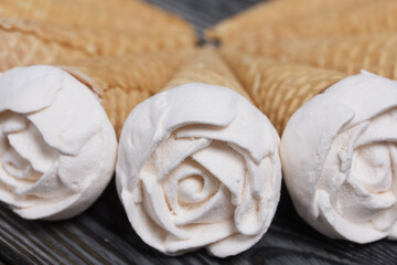 Homemade marshmallows are spread out on the table surface. Zephyr in a waffle cone. Made in the shape of a rose. Close-up shot.