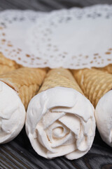 Homemade marshmallows are spread out on the table surface. Zephyr in a waffle cone. Made in the shape of a rose. Close-up shot.