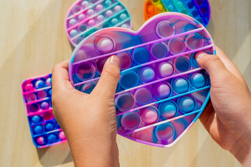 Little child playing with anti stress sensory pop it at wooden table. Hands holding and playing popit rainbow color. Trend of the 2021 year. Top view