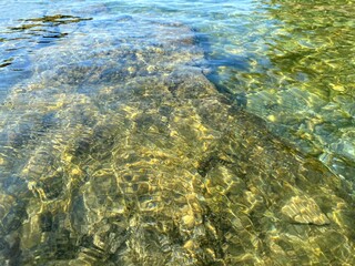 Jade green sea water pebbles beach. Transparent sea water background of rocky coast. Clear shiny ocean water. Beautiful summer seascape. Magical pebbles stones gravel on seabed. Relax, zen, harmony. 