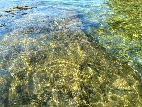 Jade green sea water pebbles beach. Transparent sea water background of rocky coast. Clear shiny ocean water. Beautiful summer seascape. Magical pebbles stones gravel on seabed. Relax, zen, harmony. 