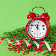Alarm clock  confetti, and tree branches on green paper background. 5 minutes before the New Year.
