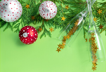 Multicolored Christmas balls  with tree branches and glasses of champagne on green paper background. New Year creative greeting card.