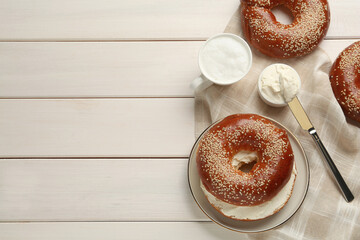 Delicious bagel with cream cheese and coffee on white wooden table, flat lay. Space for text