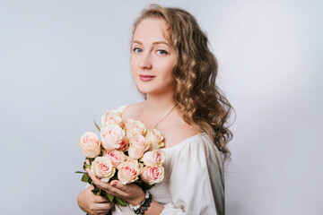 A beautiful young woman in white clothes is holding a large bouquet with pink roses. Portrait of a girl on a white background