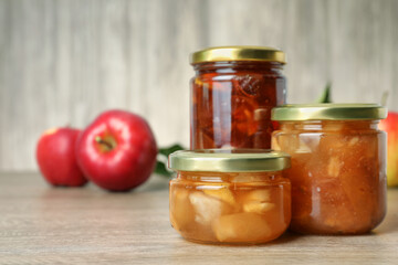 Tasty apple jam in glass jars on wooden table, space for text