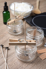 Glass jars with wicks and clothespins as stabilizers on wooden table. Making homemade candles